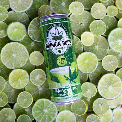 A can of Drinkin' Buds Margarita Double Shot with 10mg THC and CBD lies on a vibrant bed of sliced limes.