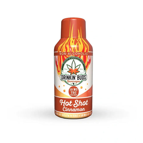 A standalone bottle of Drinkin’ Buds Hot Shot Cinnamon against a white background. The bottle is red and orange with flame graphics, a cannabis leaf logo, and text stating 10mg THC and 10mg CBD per shot