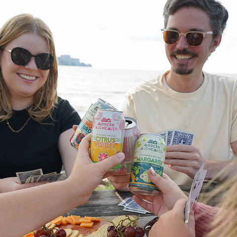 People smiling and holding Variety Pack of Modern Alchemist Cannabis Infused Mocktails including Citrus Spritz, Jungle Bird, and Margarita. Alcohol free.