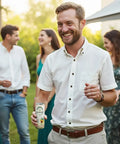 A smiling man holding a can of Drinkin’ Buds Piña Colada stands in a garden gathering with friends.