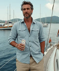 A man holding a can of Drinkin' Buds Piña Colada Double Shot stands on a sailboat, with other boats and people in the background.