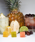 Two cocktails with a pineapple, lemon, lime, and cherry on a white background