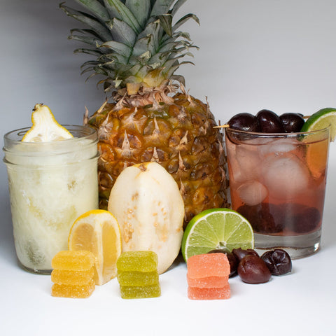 Two cocktails with a pineapple, lemon, lime, and cherry on a white background