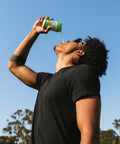 Person drinking from a can of THC IPA against a clear blue sky