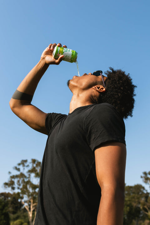 Person drinking from a can of THC IPA against a clear blue sky