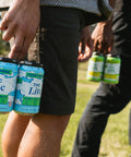Person holding cans of 'THC Lite' brew in a park setting