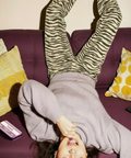 Person lying on a purple couch with zebra-striped leggings and gray sweatshirt eating a Happly gummy.