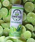 The image features a "Drinkin' Buds Beverages" Margarita can placed on a bed of fresh lime slices. The label highlights a cannabis leaf, the slogan "Taste the New Buzz," and a margarita graphic, emphasizing a cool, citrus-infused experience.