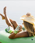 The image shows a woman lounging on an inflatable raft in a lake, wearing a straw hat and holding a "Drinkin' Buds Beverages" Margarita can. The scene conveys a relaxed, carefree vibe, perfect for enjoying a refreshing cannabis-infused drink outdoors.
