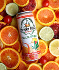 The image features a "Drinkin' Buds Beverages" Rum Punch can surrounded by vibrant slices of blood oranges, limes, lemons, and red cherries. The colorful arrangement emphasizes the drink's fruity, tropical flavors infused with cannabis.