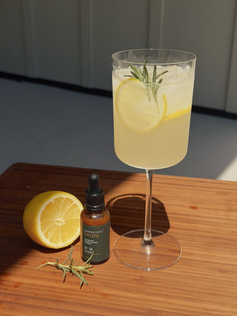 Lemon spritz with rosemary next to a bottle of Sober(ish) Drops