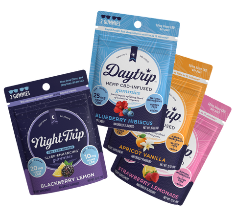 Sample pack showing a stack of 4-pack packaging renders of all four flavors of gummies: Night Trip CBD + CBN-infused blackberry lemon, Daytrip blueberry hibiscus CBD-infused, Daytrip apricot vanilla CBD-infused, and Daytrip strawberry lemonade CBD-infused