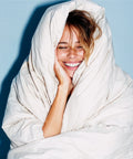 Woman wrapped in a white blanket, smiling against a light blue background