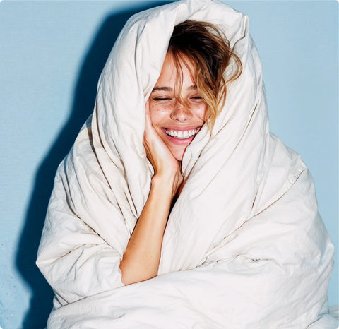 Woman wrapped in a white blanket, smiling against a light blue background